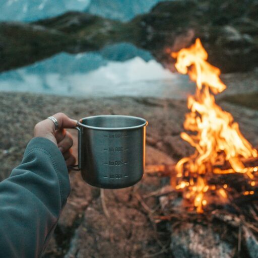 Coffee cup with campfire beside a lake.